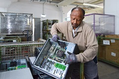 Ein Mann steht vor einer Kiste mit Elektroschrott und hält einen alten Computer in den Händen
